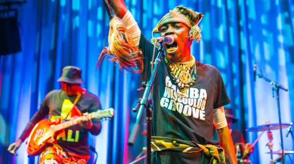 Bamba Wassoulou Groove performing at globalFEST/APAP|NYC 2025. Singer is wearing a beaded necklace and hat and has one hand up in the air. In the background, the guitarist just finished strumming a chord.