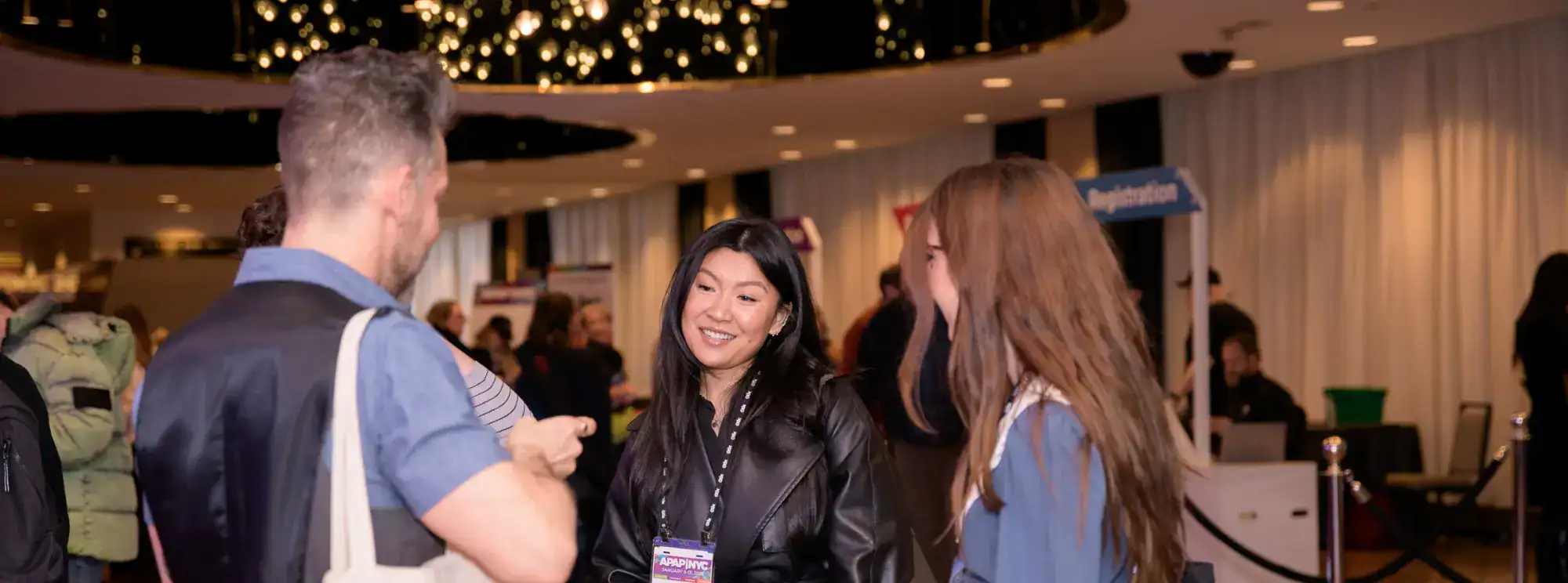 People with conference badges mingling in front of registration booths in a lobby.